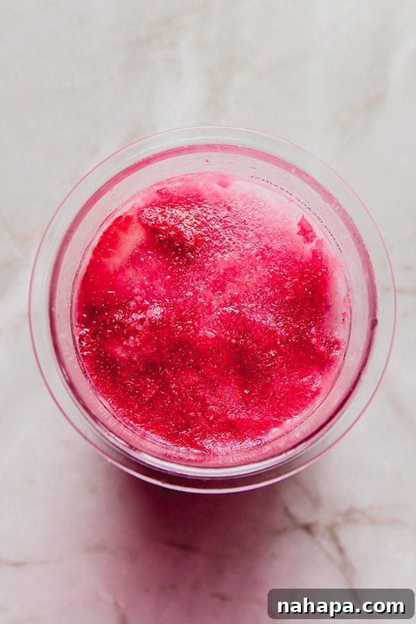 Pouring coconut milk and juices over strawberries in the Ninja Creami pint.