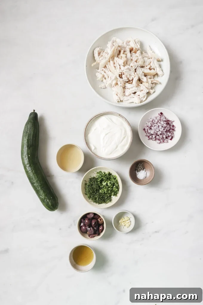 A bowl of fresh ingredients for Tzatziki Chicken Salad, including shredded chicken, herbs, olives, and grated cucumber.