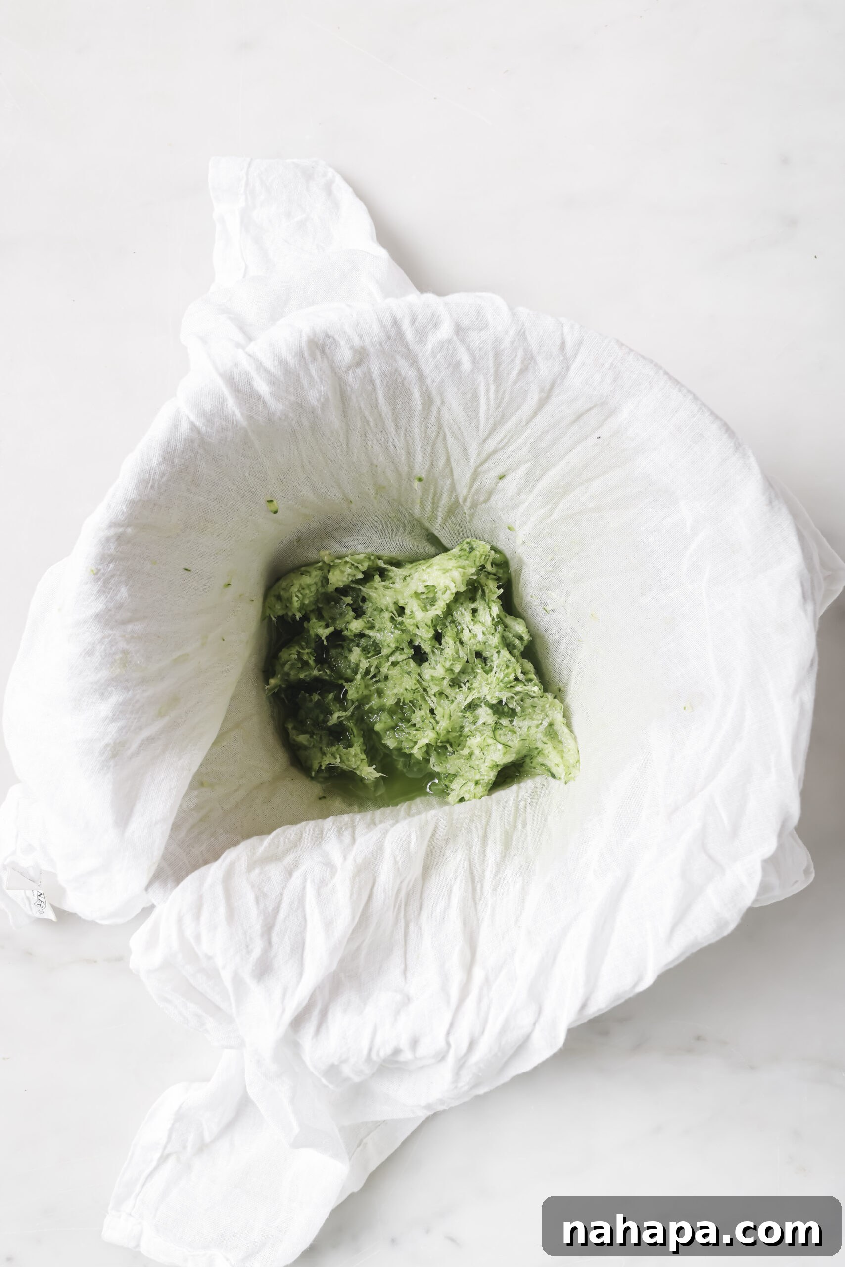 Grated cucumber being squeezed in a cheesecloth to remove excess water for tzatziki.