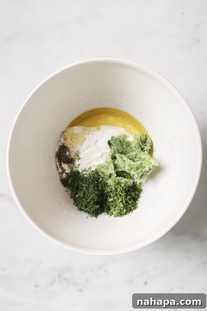 Ingredients for tzatziki sauce, including yogurt, lemon, and herbs, being mixed in a bowl.