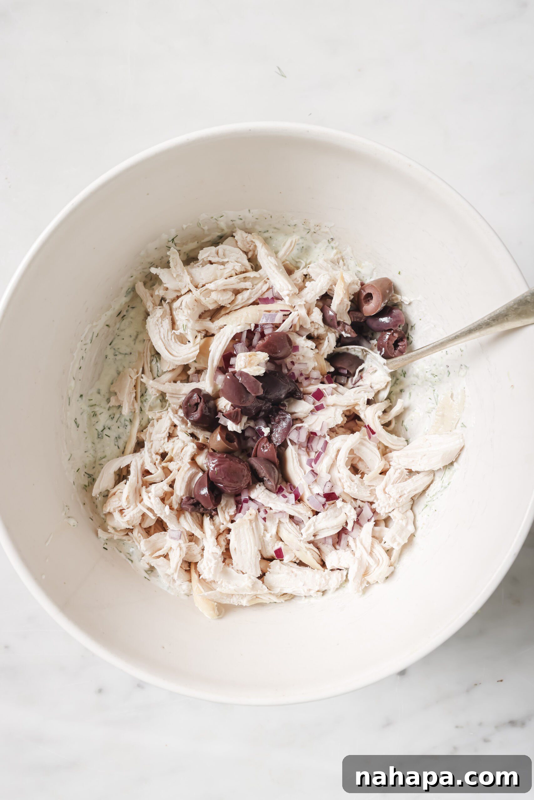 Shredded chicken, red onion, and kalamata olives being added to the tzatziki mixture.