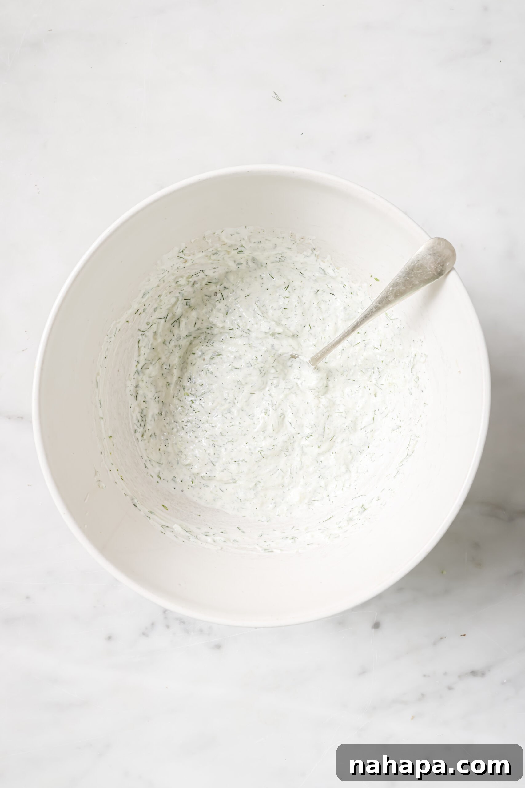 Tzatziki chicken salad being mixed in a bowl, showing the even coating of dressing.