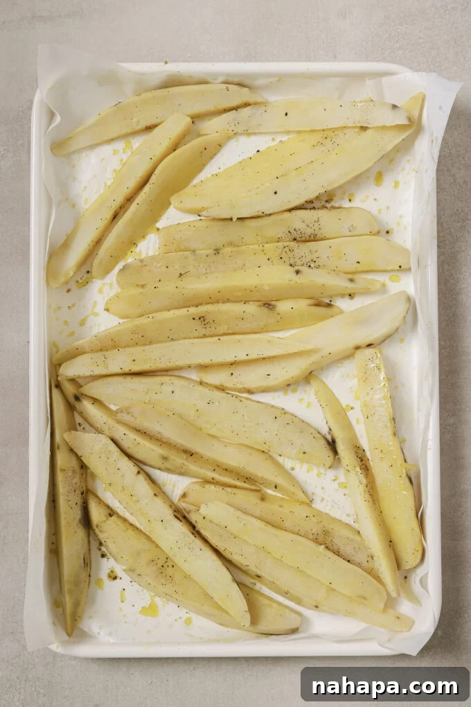 Thoroughly dried Japanese sweet potato fries laid out on a parchment-lined baking sheet, seasoned with oil, salt, and pepper.