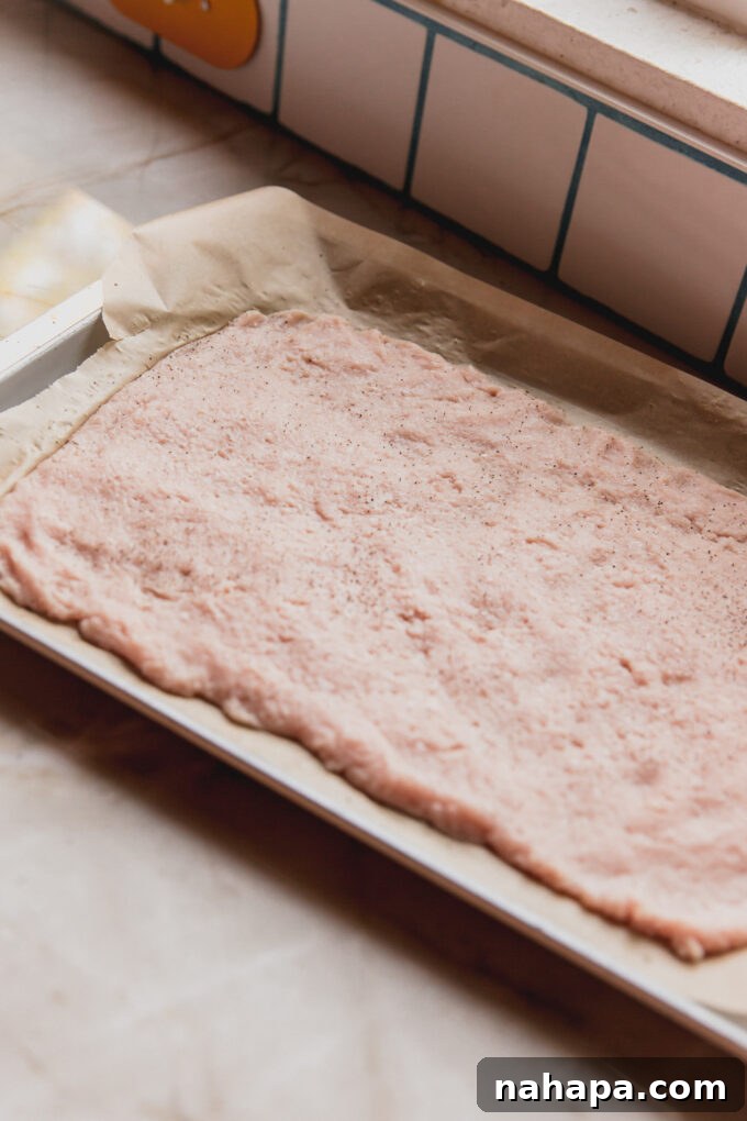 Flattened ground chicken on a lined baking sheet.