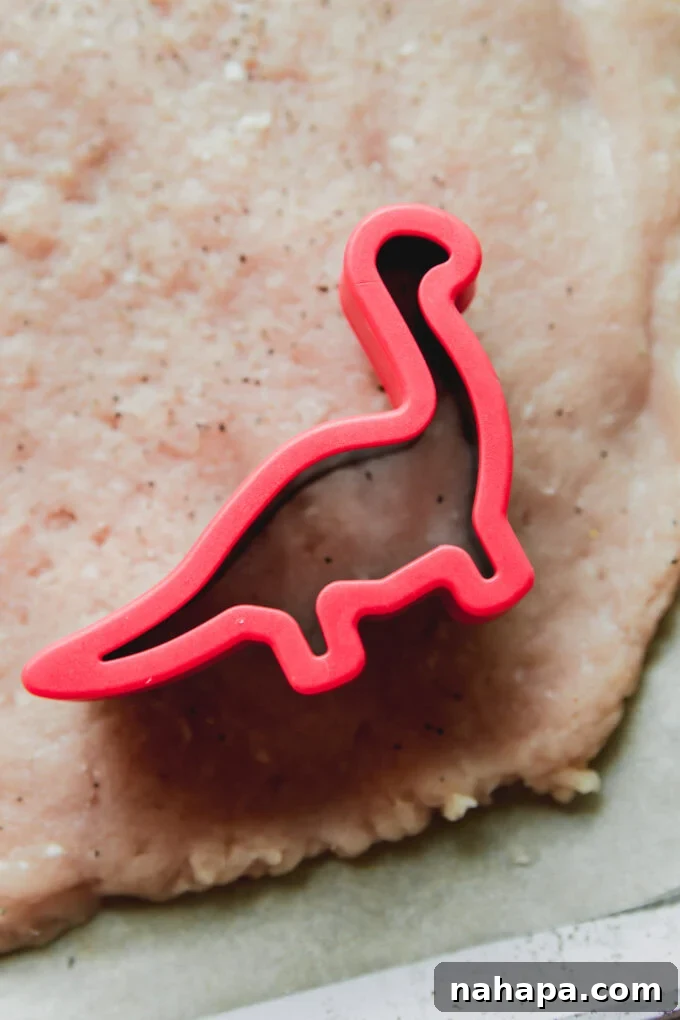 Red dinosaur-shaped cutter on flattened ground chicken.