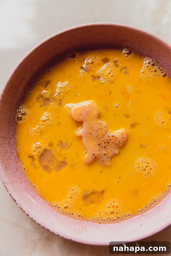 Dino-shaped chicken in a bowl of egg wash.