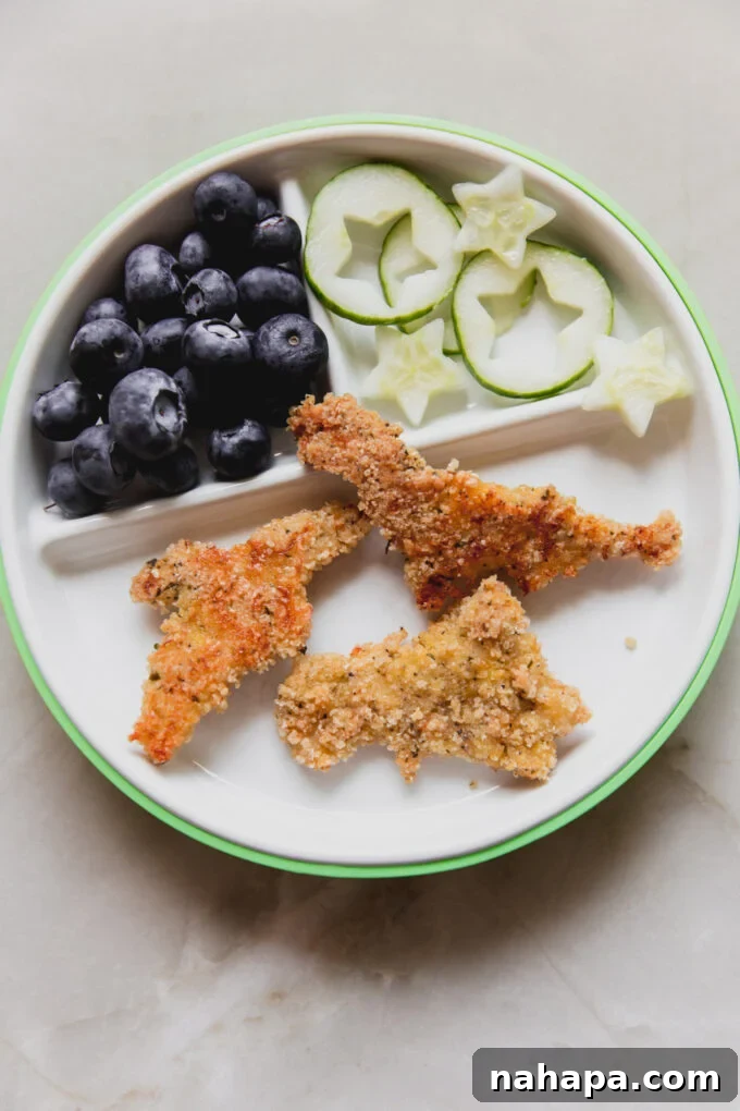 Gluten-free dino nuggets on a plate with cucumbers and blueberries.