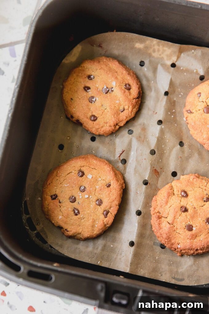 Perfectly baked, golden-brown air fryer chocolate chip cookies on parchment paper inside an air fryer basket, ready to be enjoyed.