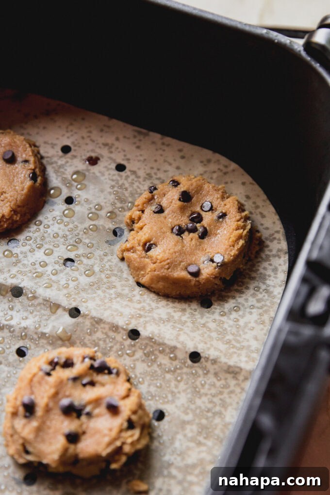 Uncooked air fryer chocolate chip cookies neatly placed on parchment paper within the air fryer basket, waiting to be cooked.