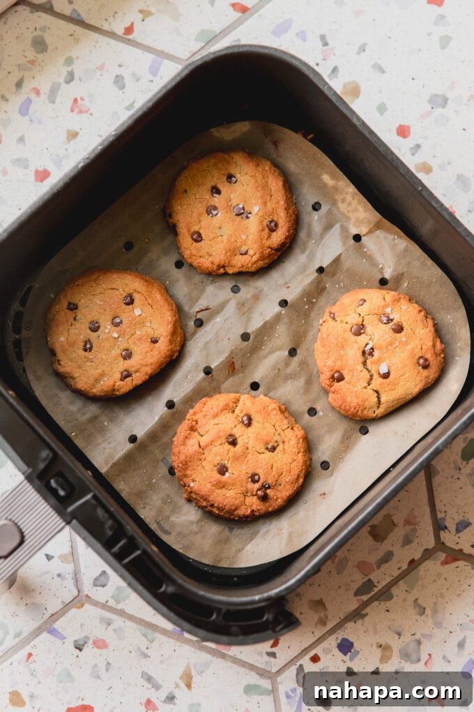 Freshly baked air fryer chocolate chip cookies, golden and complete, resting on parchment paper in the air fryer basket.