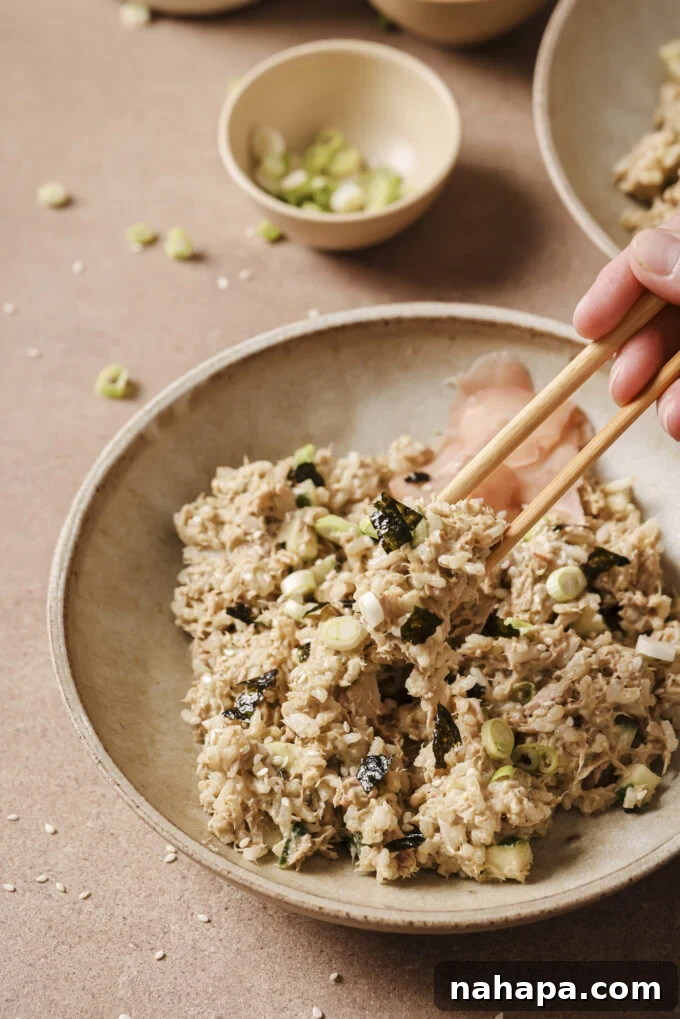 Chopsticks picking up a helping of avocado tuna rice from the bowl.