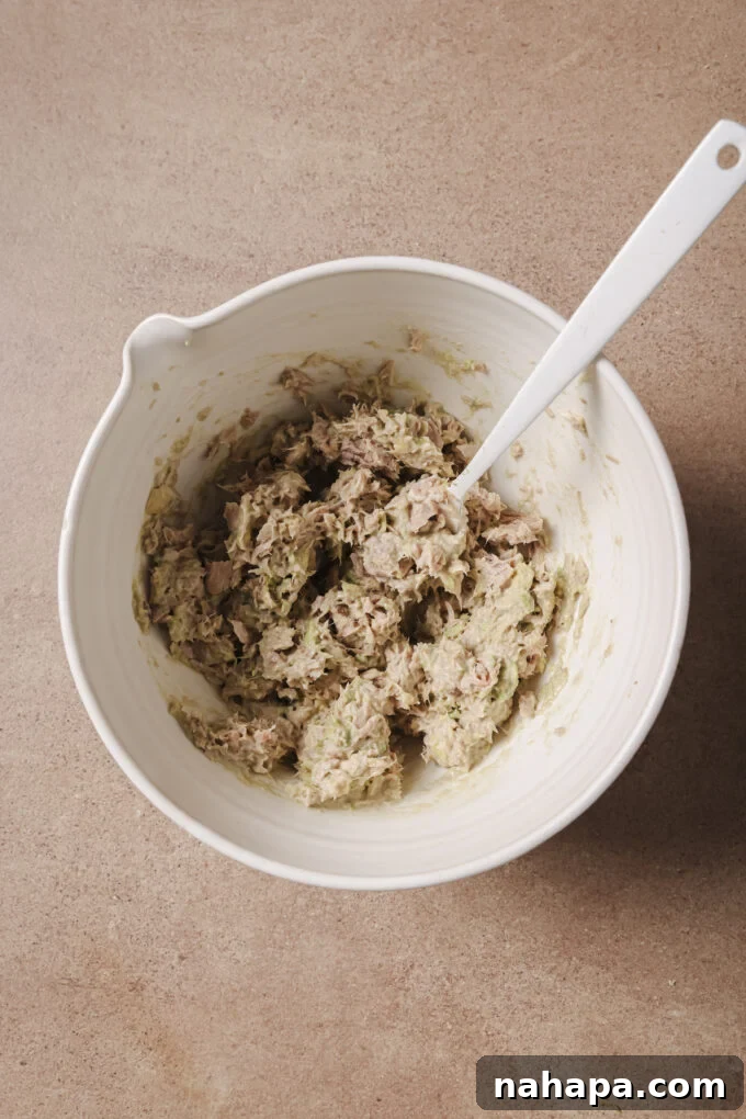 Avocado and tuna being mixed in a white bowl with a spoon.