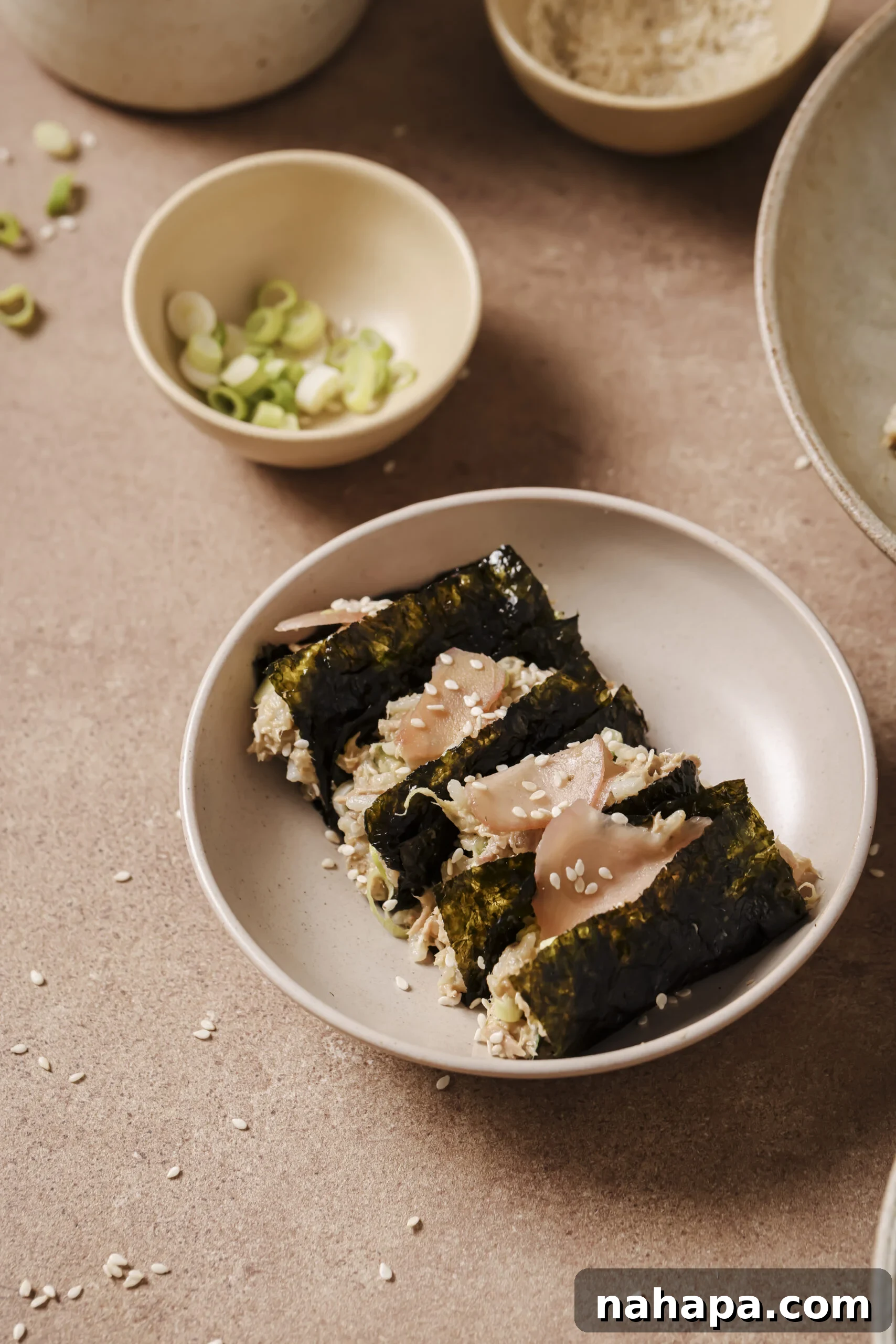 Four avocado tuna rice seaweed wrappers on a plate next to a bowl with green onion.