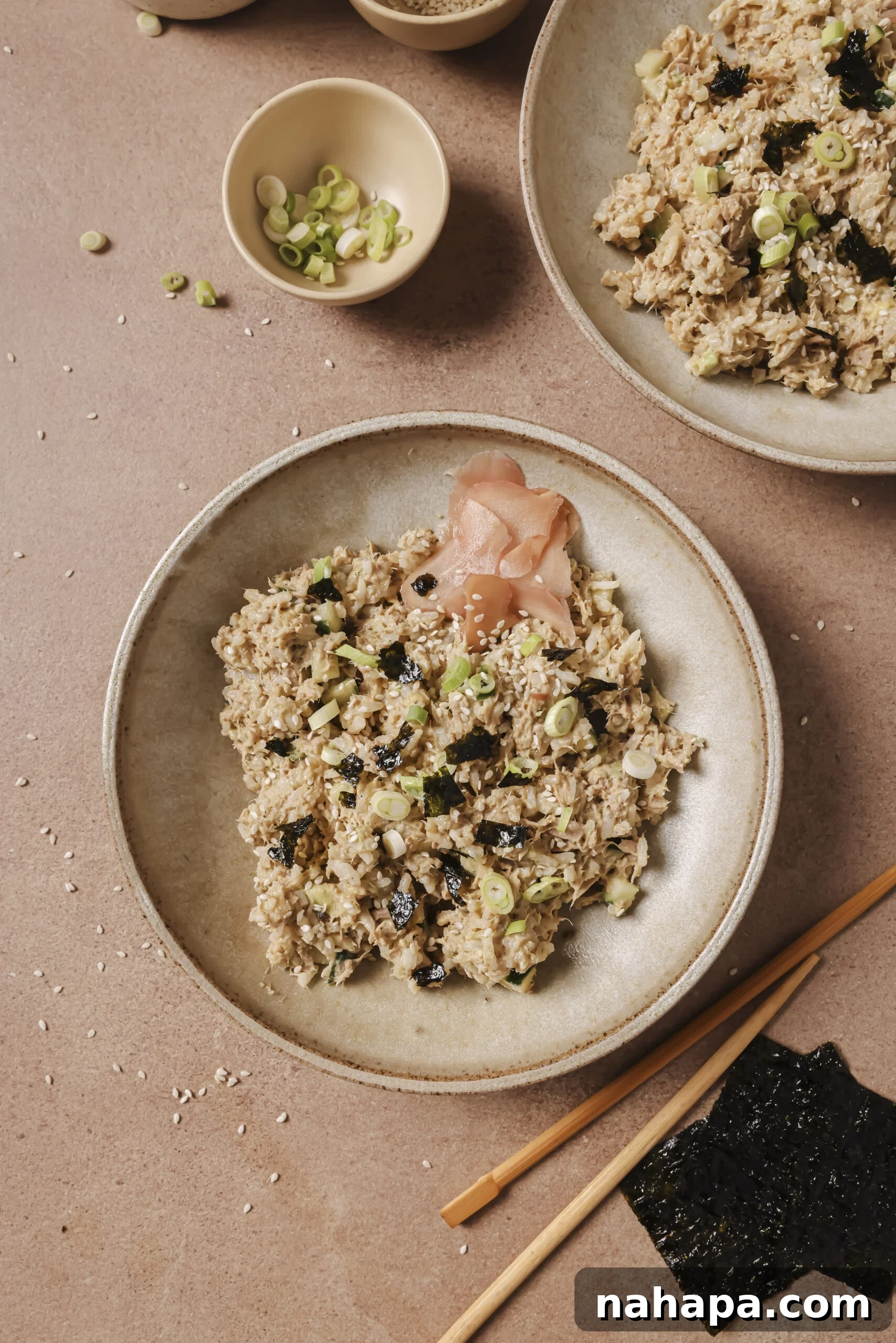 Avocado tuna rice bowl in a beige bowl and topped with pickled ginger on the side.