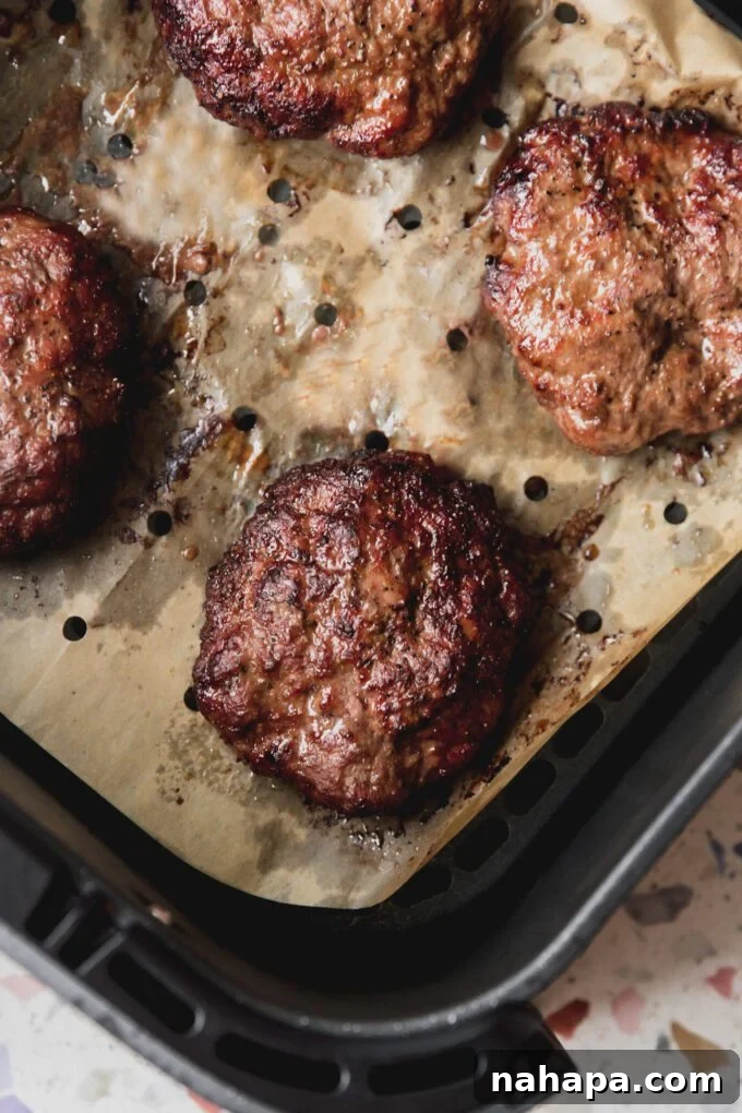 Air fryer burgers cooked to perfection in the air fryer, nestled on vented parchment paper, ready to be served.