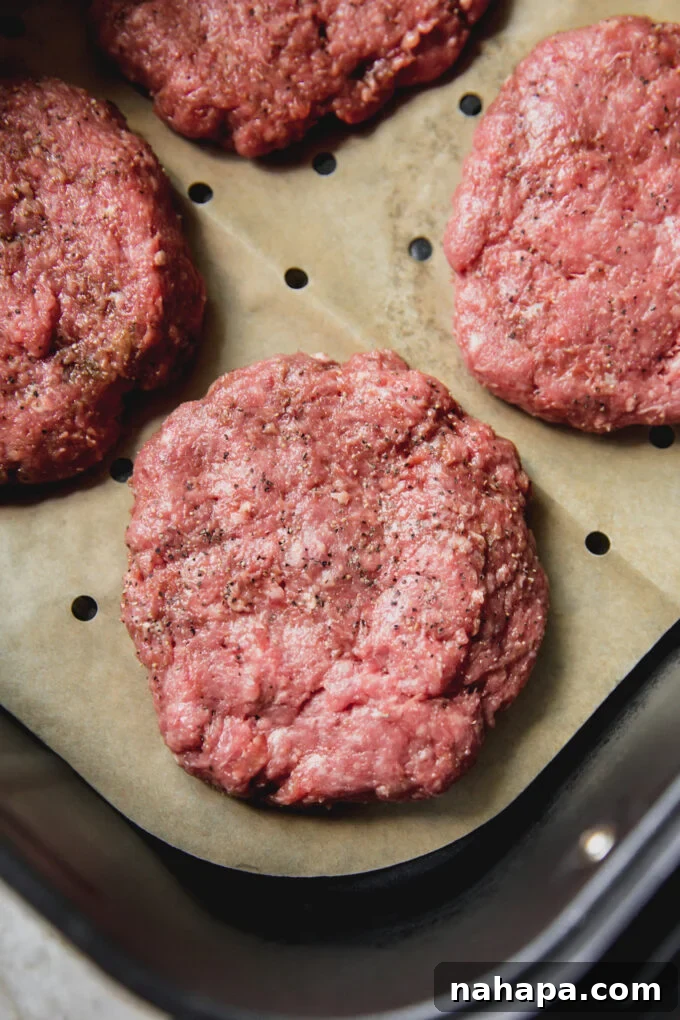 Air fryer burgers, lightly seasoned and uncooked in the air fryer with vented parchment paper, before cooking.