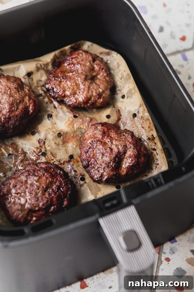 Two perfectly cooked air fryer burgers resting on vented parchment paper in the air fryer basket after cooking.