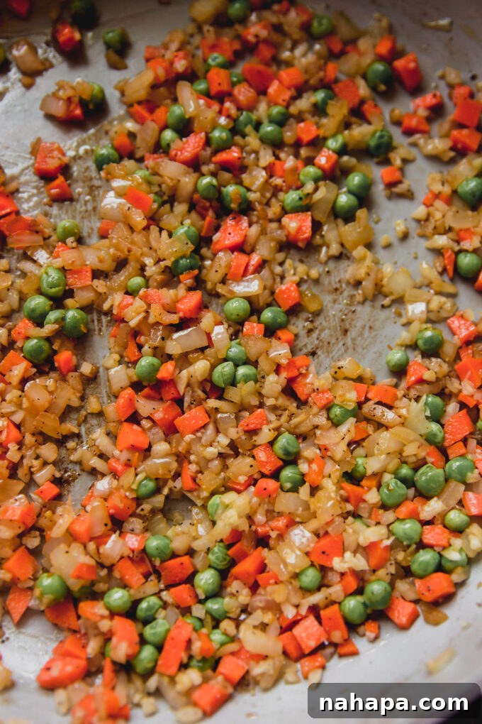 Carrots, onion, cauliflower rice and peas cooking in a pan.