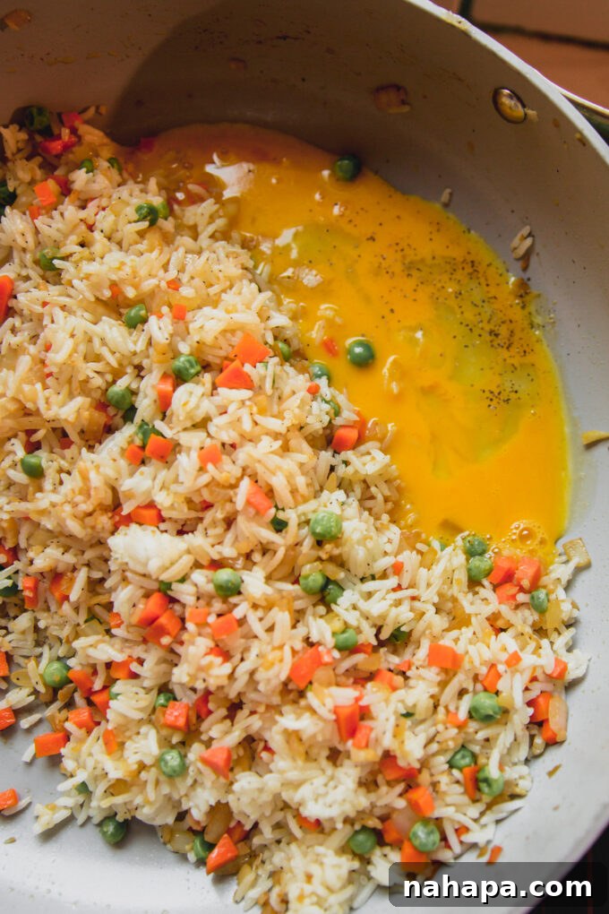 Fried rice cooking in a pan with raw scrambled eggs poured in.