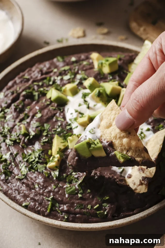 Refried beans topped with avocado and being dipped with a tortilla chip.