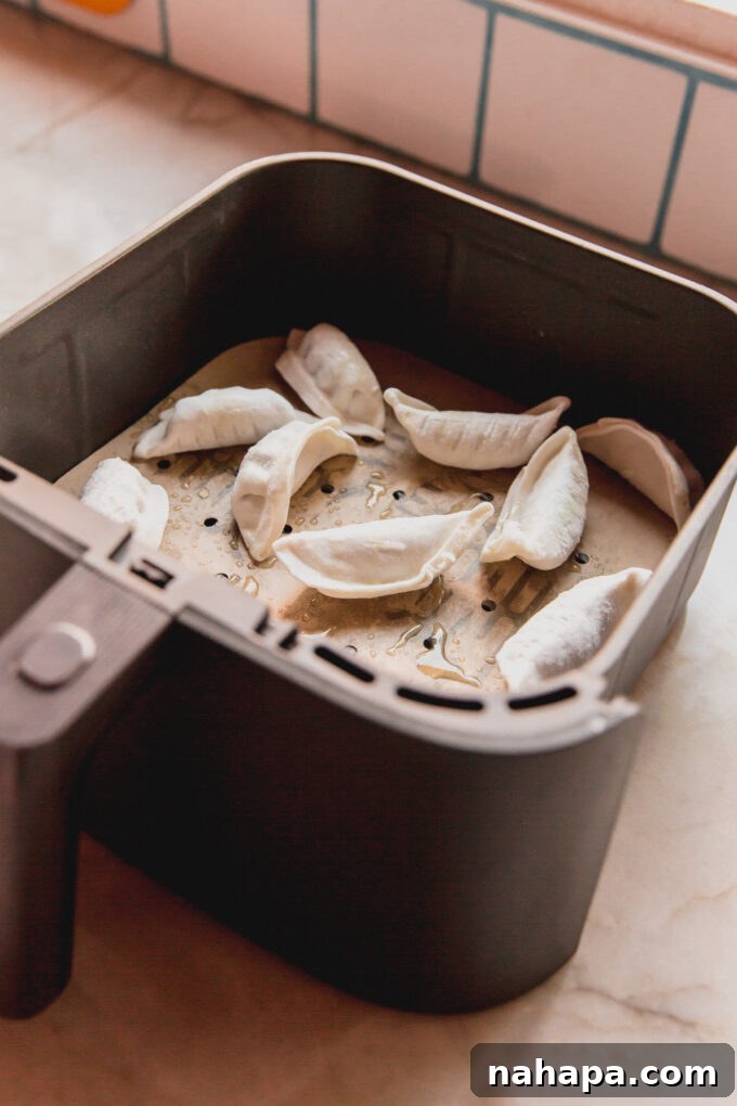 Gluten free dumplings uncooked, arranged in a single layer in an air fryer basket lined with parchment paper.