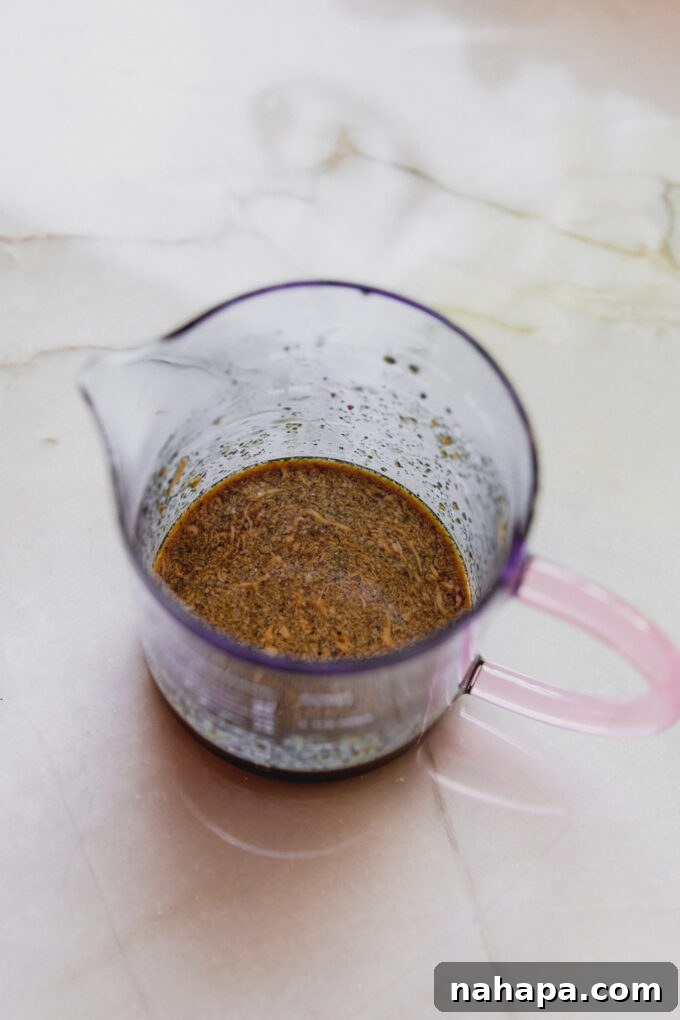 A glass measuring cup holding the freshly whisked coconut aminos based dressing, ready to be poured over the salad.
