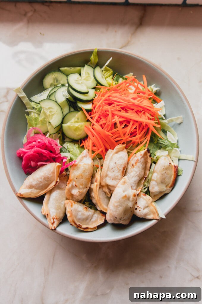 A large bowl filled with potstickers, fresh lettuce, shredded carrots, chopped cucumber, and vibrant red onion, before dressing is added.