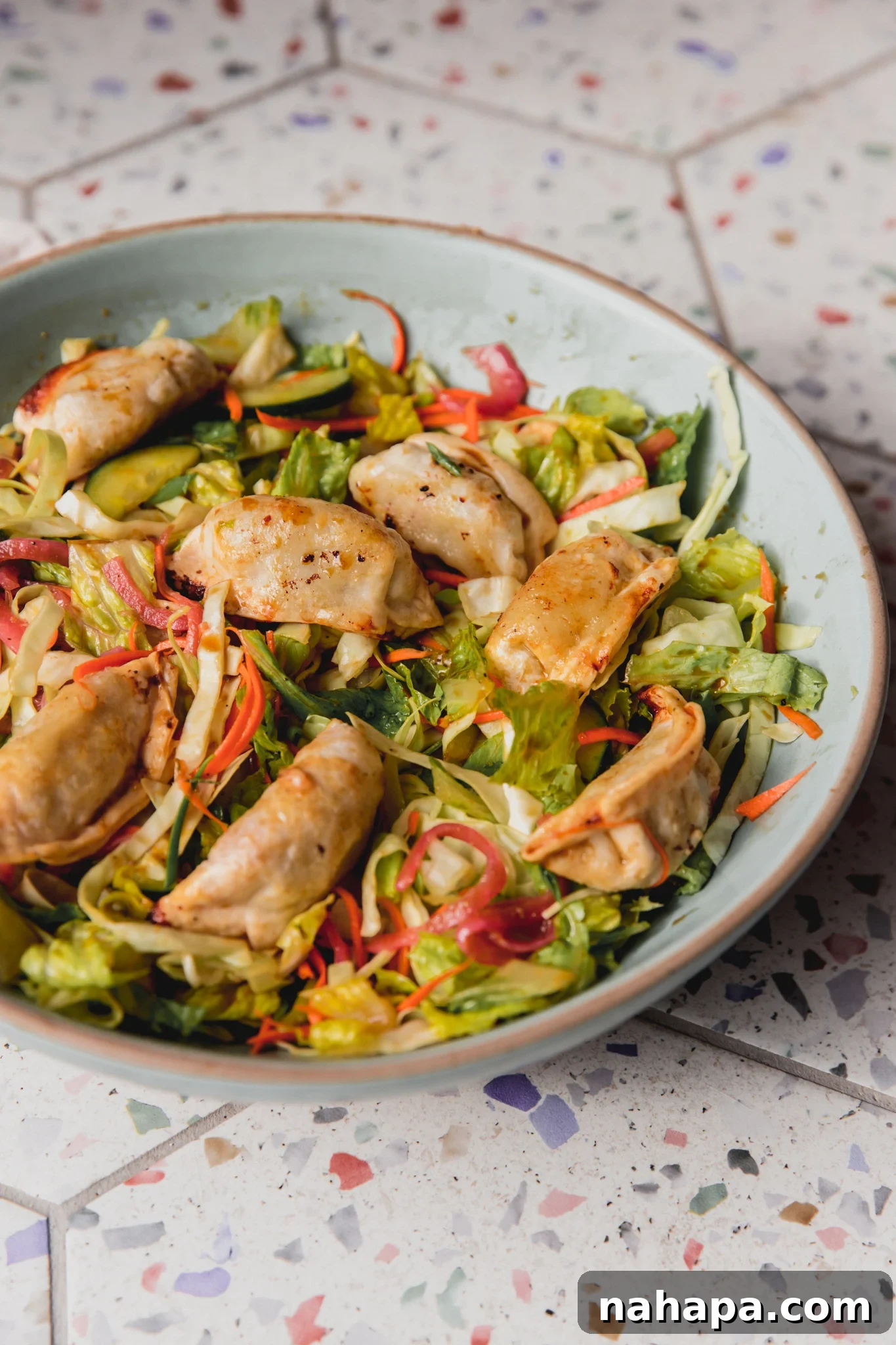 Dumping salad in a large bowl with veggies and dumplings.
