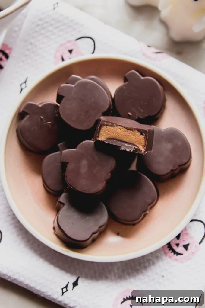 Almond butter cups shaped like festive pumpkins on a pink plate, one with a bite taken revealing the creamy filling.