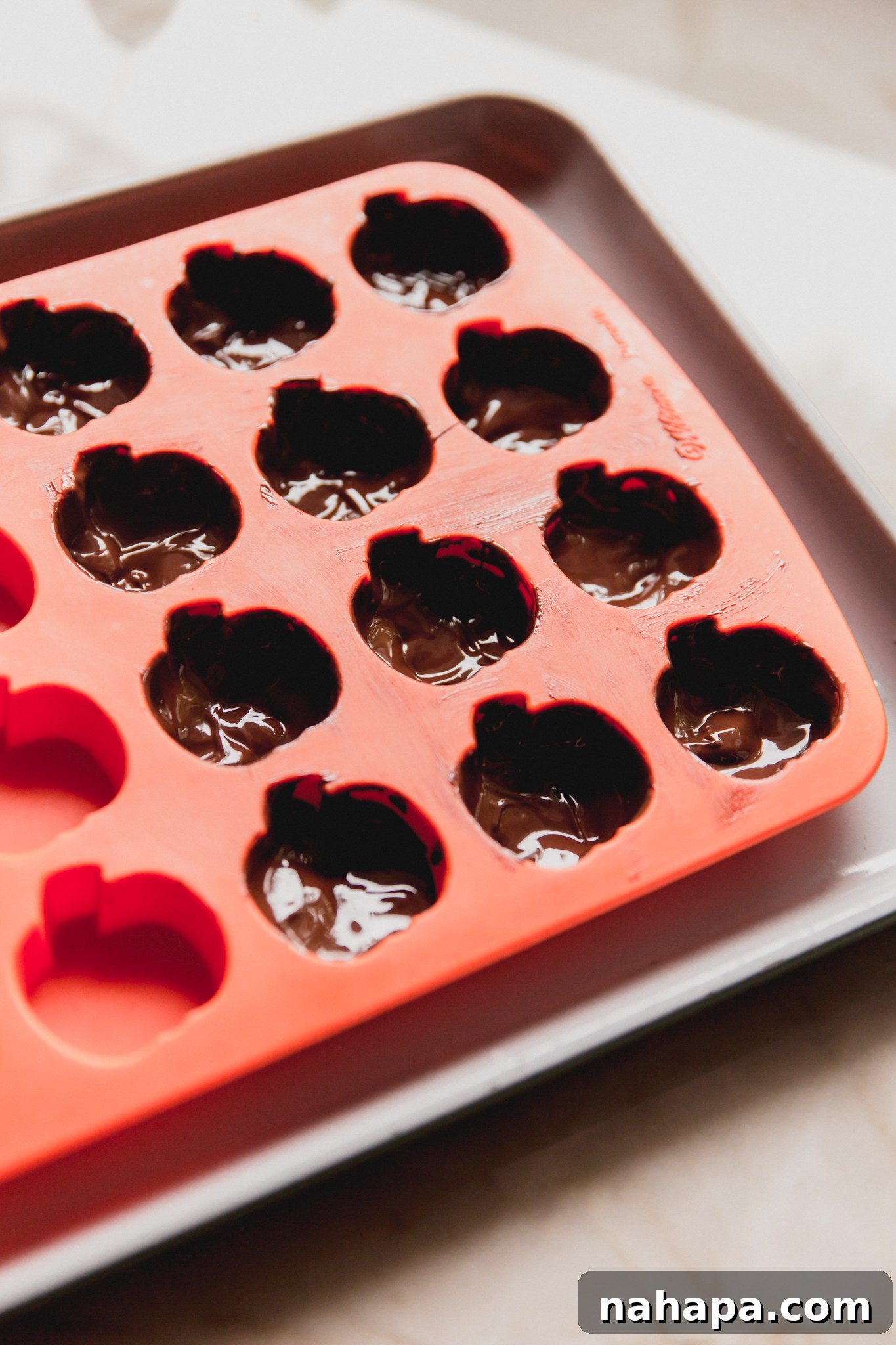 Pumpkin mold with a melted chocolate coating on the inside of 12 cavities, forming the base layer.