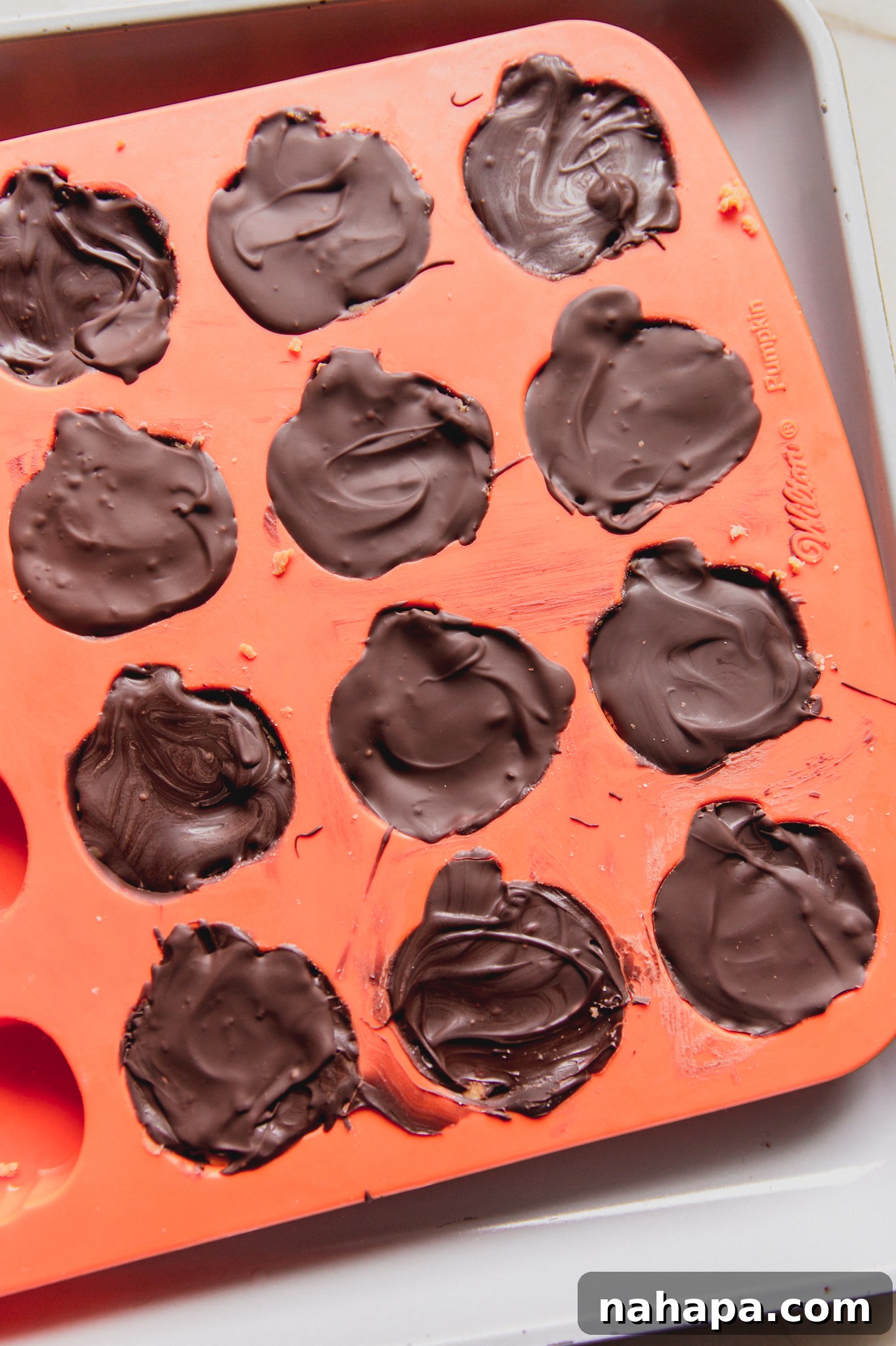 Mini almond butter Reese's cups assembled in a pumpkin mold, fully covered with chocolate and ready to set.