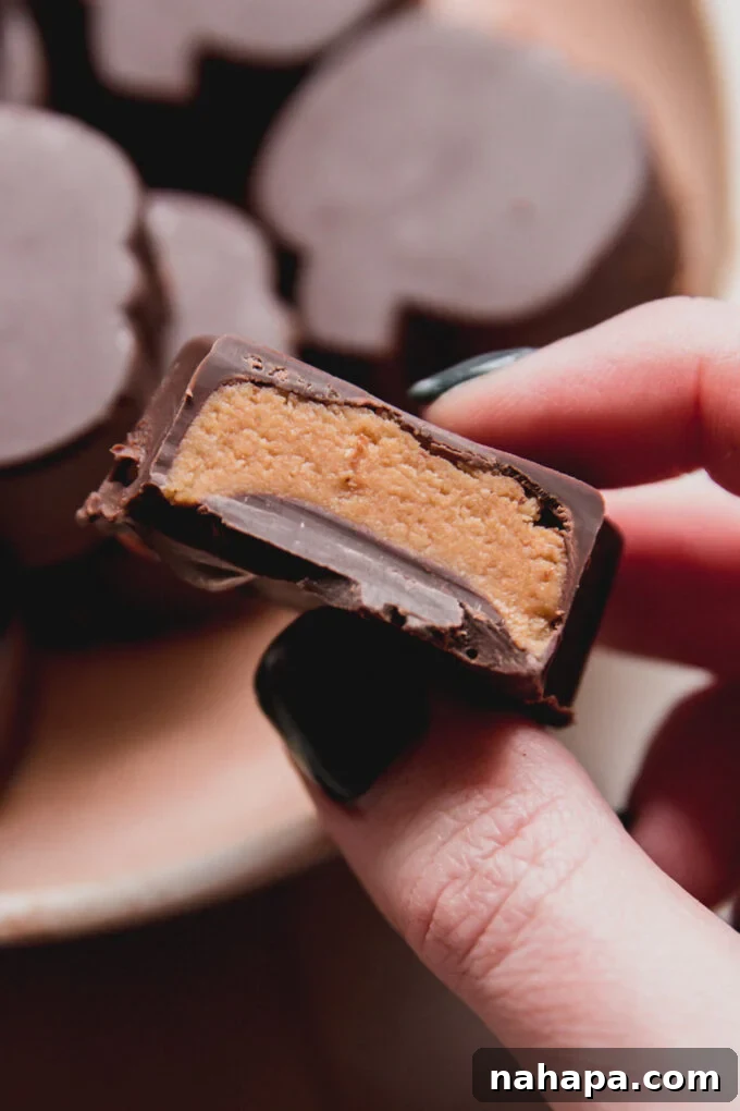 An almond butter cup with a bite taken, held up to showcase the creamy filling nestled within the rich chocolate shell.