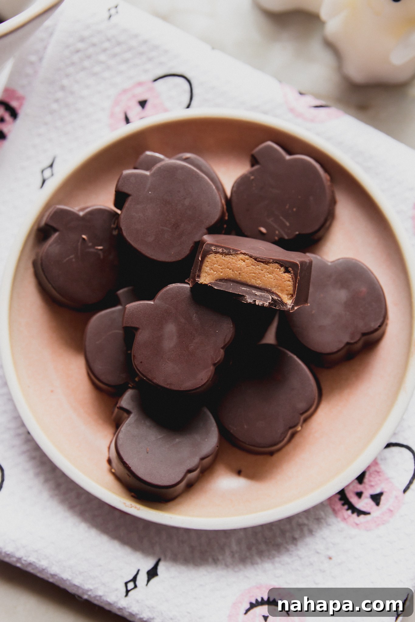 Almond butter cups shaped like pumpkins on a pink plate, with a bite taken from one, showcasing the creamy filling.