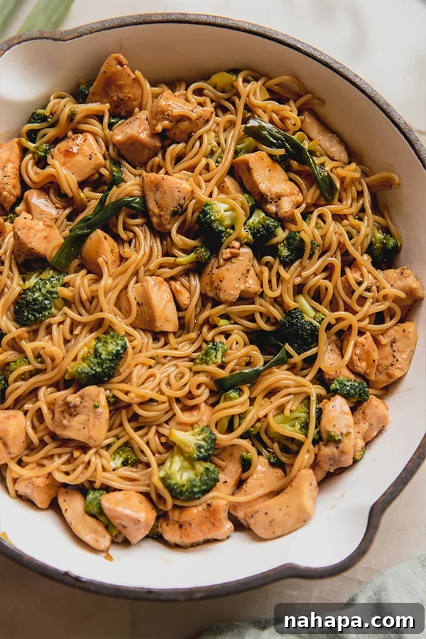 A close-up shot of a vibrant chicken and broccoli ramen stir fry, freshly cooked in a white pan, with steam gently rising, highlighting the rich sauce coating the noodles and vegetables.