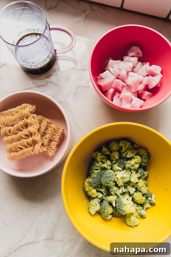 A vibrant collection of ingredients for chicken and broccoli ramen stir fry laid out in small bowls, including diced chicken, fresh broccoli florets, and gluten-free ramen noodles, ready for cooking.