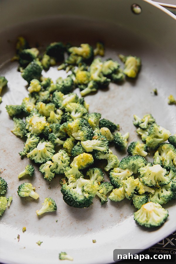 Fresh broccoli florets being expertly sautéed in a hot pan, showing their vibrant green color developing as they become tender-crisp for the stir fry.