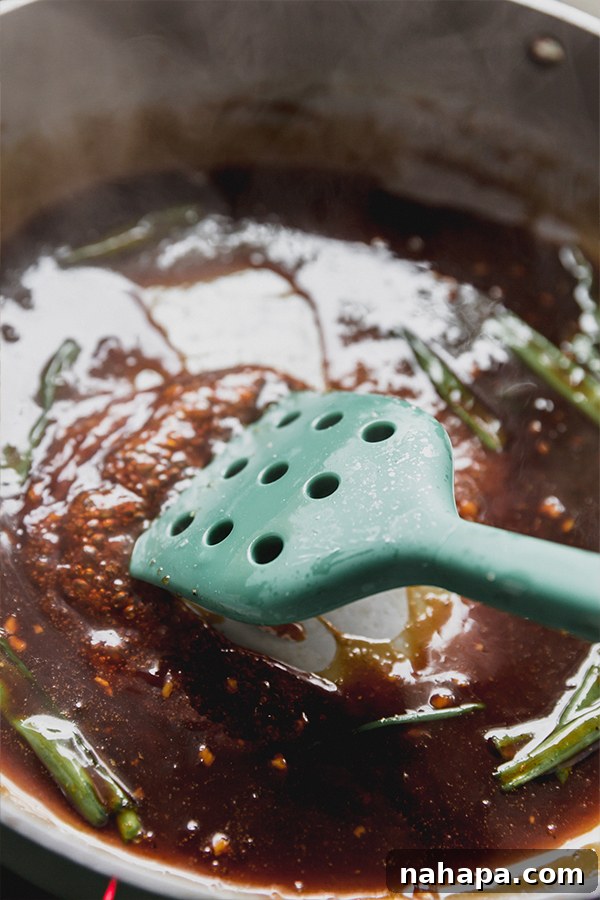 A rich, savory teriyaki-style sauce simmering to perfection in a pan, stirred with a green spatula, creating a glossy base for the stir fry.