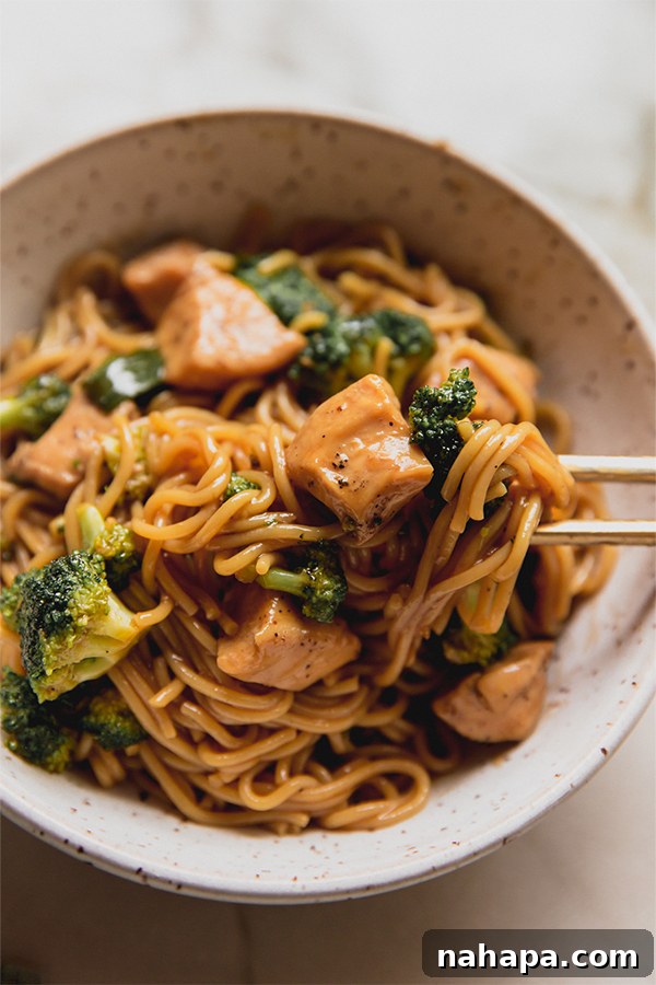 Two bowls filled with a steaming, delicious chicken and broccoli ramen stir fry, garnished with green onions and ready to be enjoyed with chopsticks.
