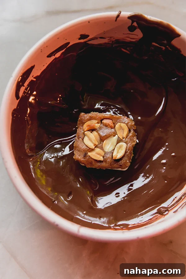 Mini snickers bars, partially dipped in melted chocolate and topped with crushed peanuts, awaiting full coating.