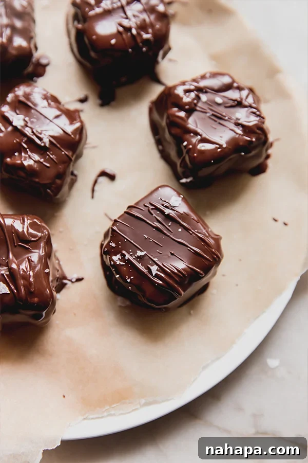 Mini snickers bars on a plate, freshly dipped in chocolate and topped with flakey sea salt, ready to set.