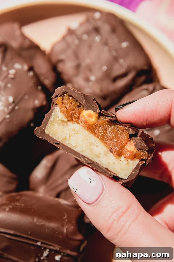 A mini snickers bar cut in half, revealing the distinct layers of light nougat, darker date caramel, peanuts, and the surrounding chocolate coating.