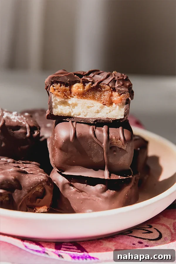 Guilt-Free Snickers Bliss 7 Three mini snickers bars on a plate, with one expertly cut in half to display the delicious inner layers of nougat, date caramel, and crunchy peanuts, all coated in chocolate.