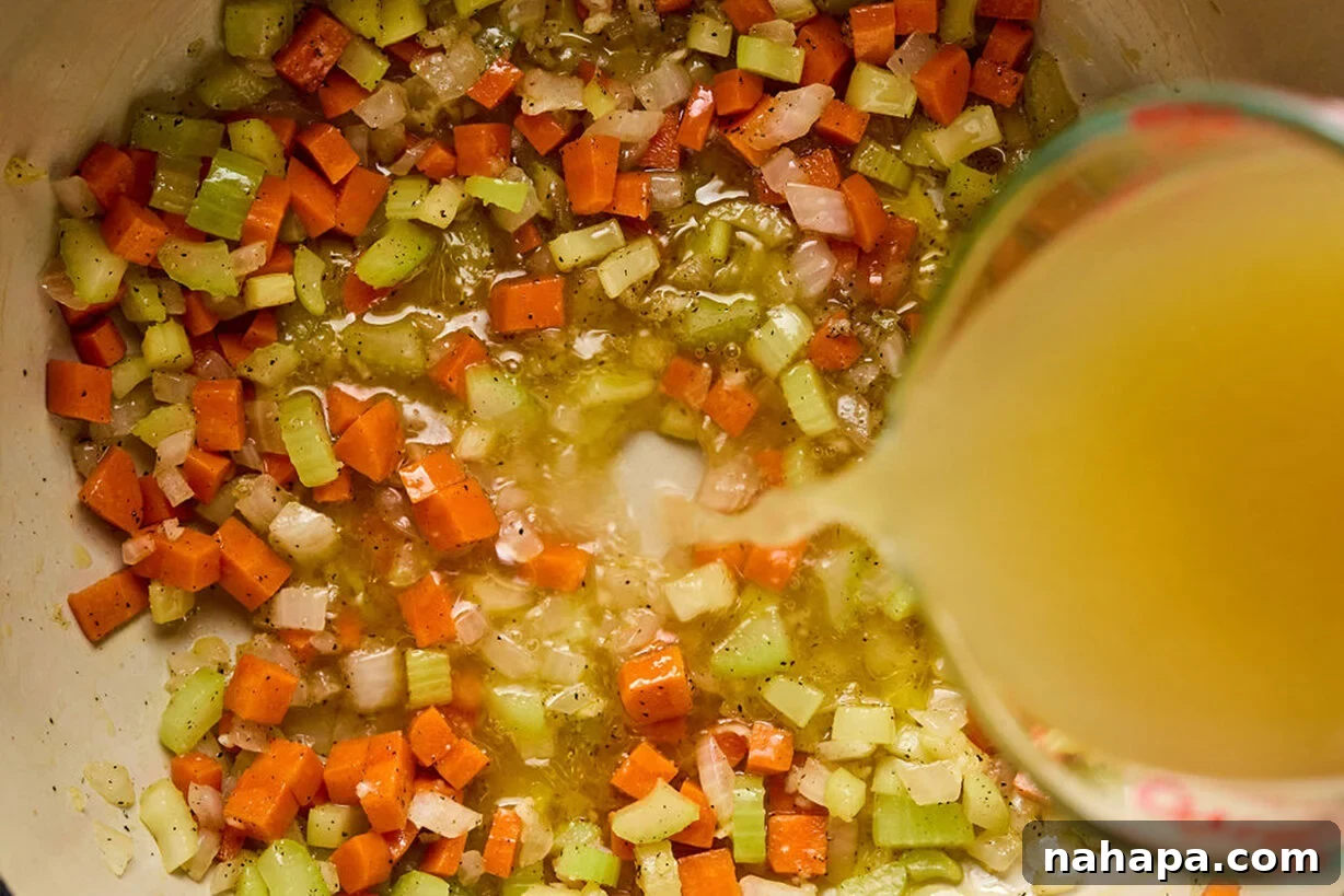 Celery, onion, and carrot sautéing in a Dutch oven, with chicken broth being poured in.