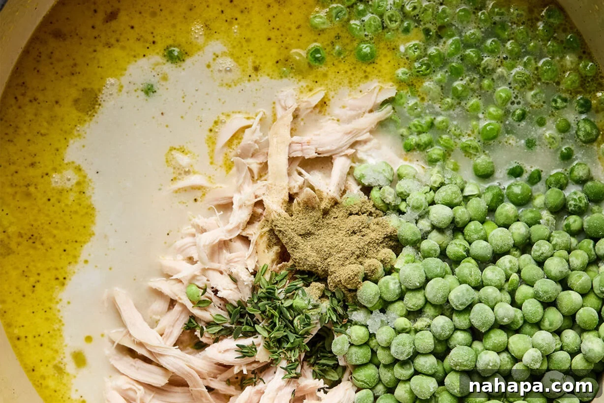 Shredded chicken and frozen peas submerged in a simmering soup broth within a pot.