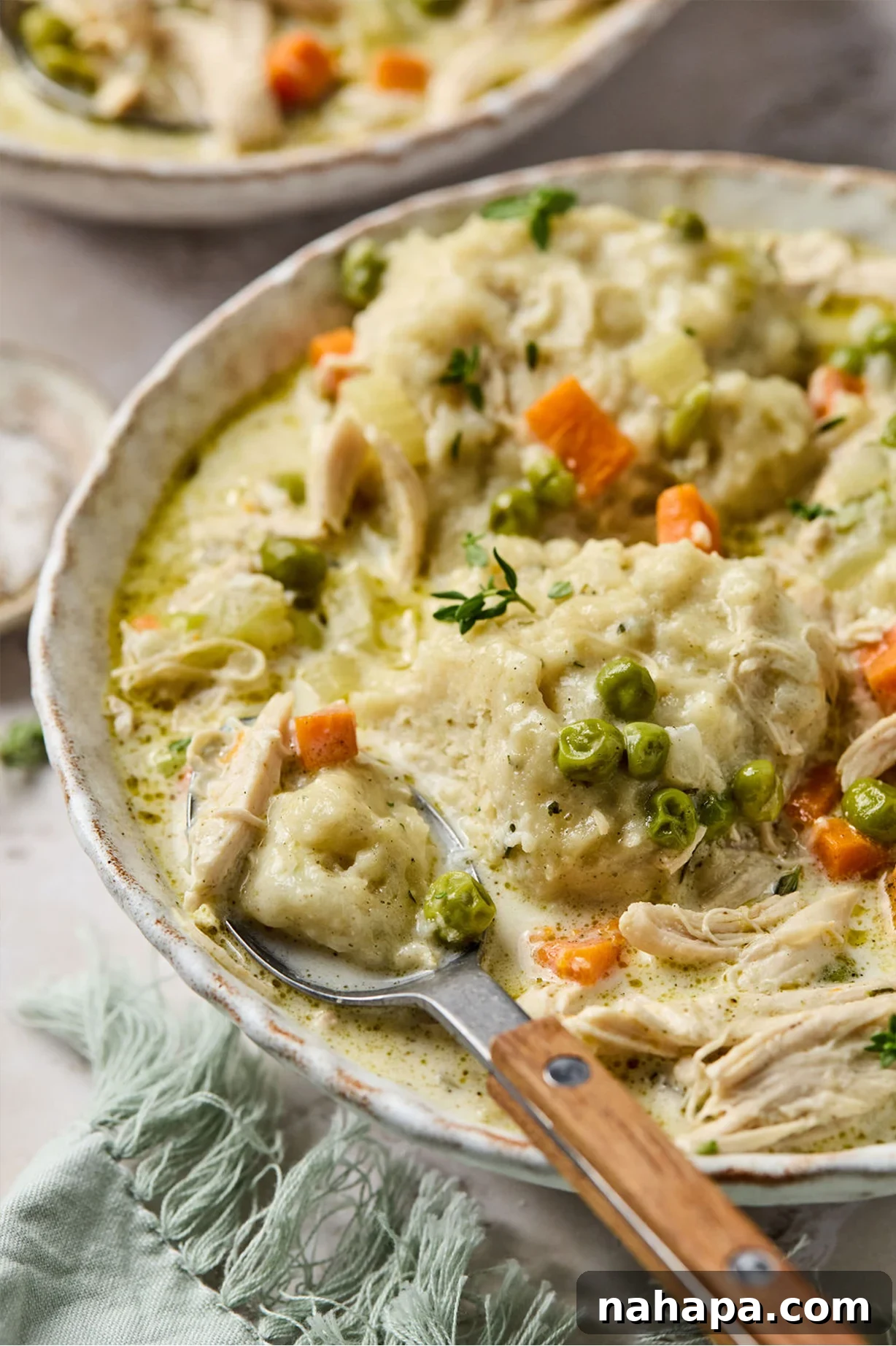 A close-up of gluten-free chicken and dumplings in a bowl, with a spoon cutting into one of the fluffy dumplings.
