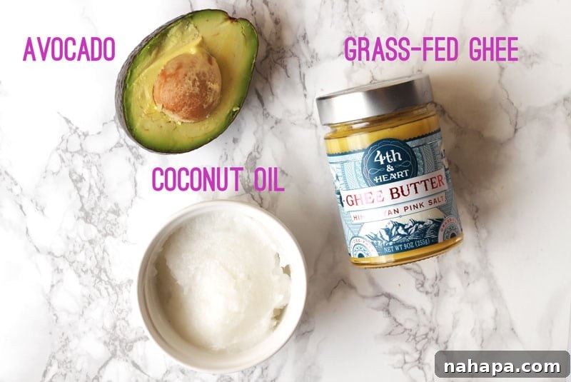 A selection of healthy fats: coconut oil, avocado, and ghee, arranged on a marble background.