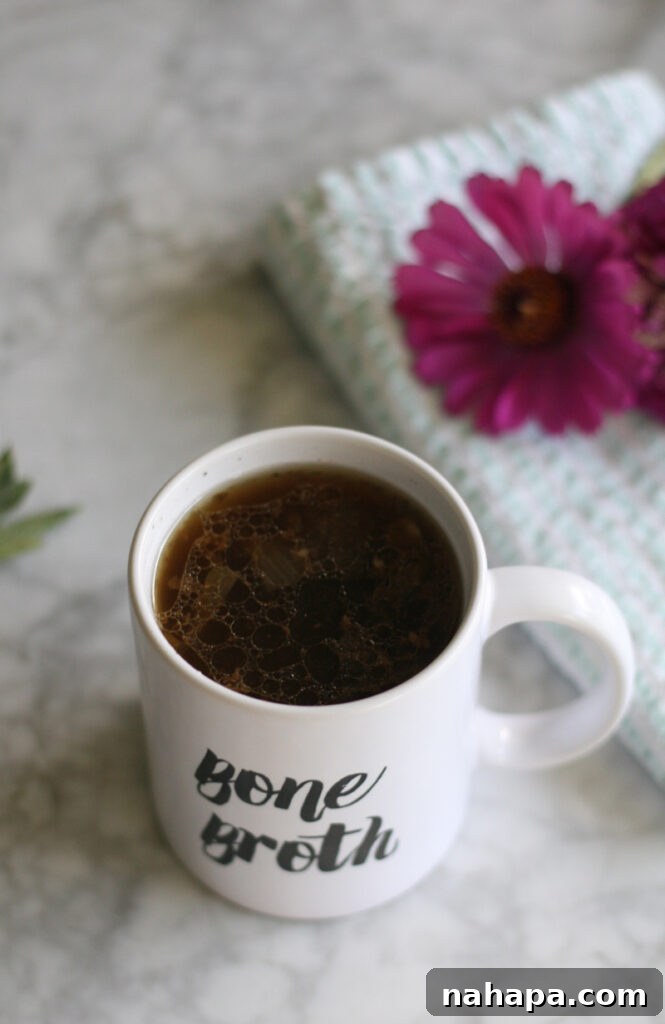 A warm cup of bone broth in a mug next to some delicate flowers.