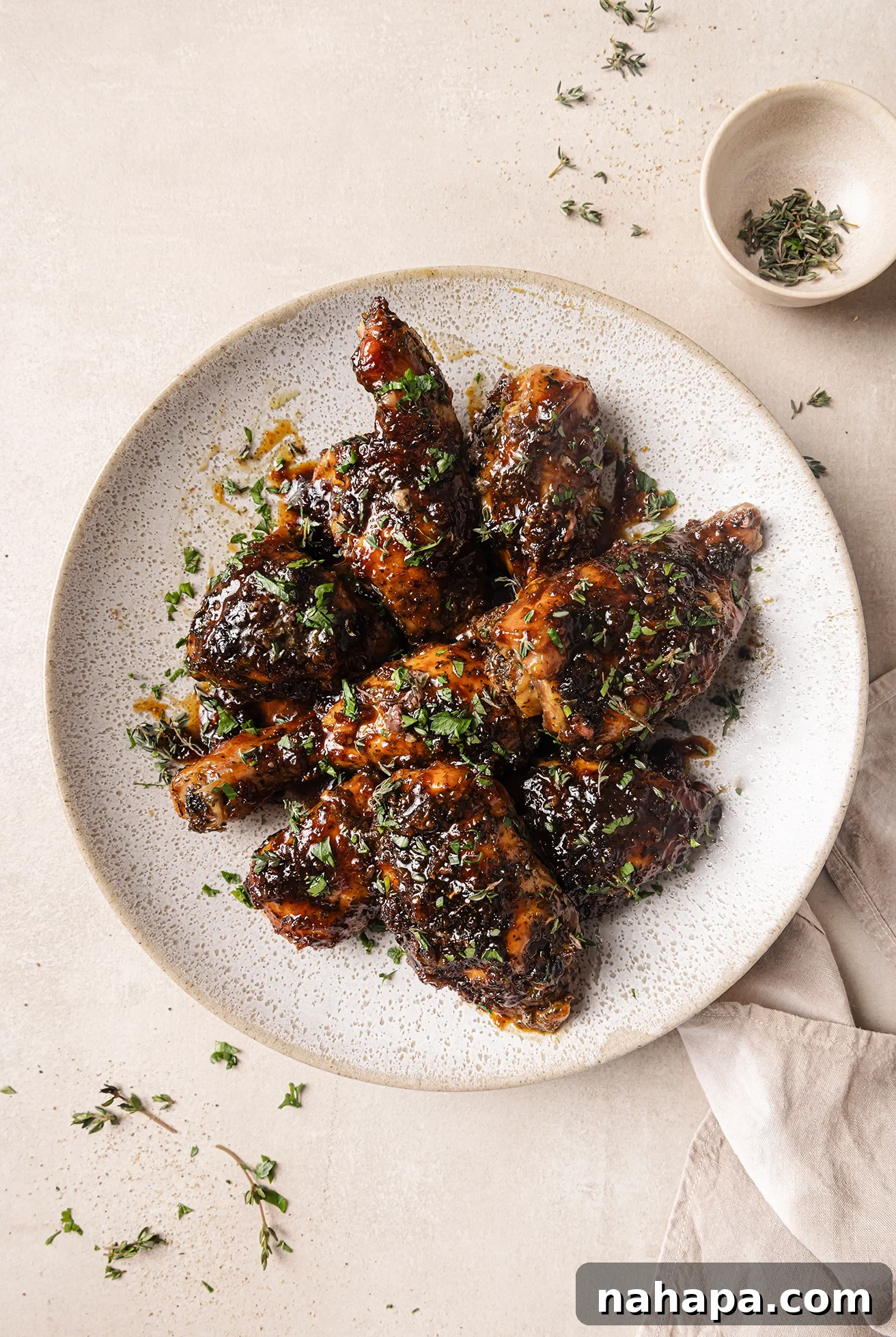 Baked turkey wings on a plate topped with thyme, with a small bowl of thyme on the side.