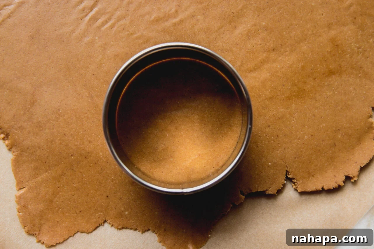 A round cookie cutter neatly pressing into a sheet of rolled-out gingerbread dough, creating circular cookie shapes.