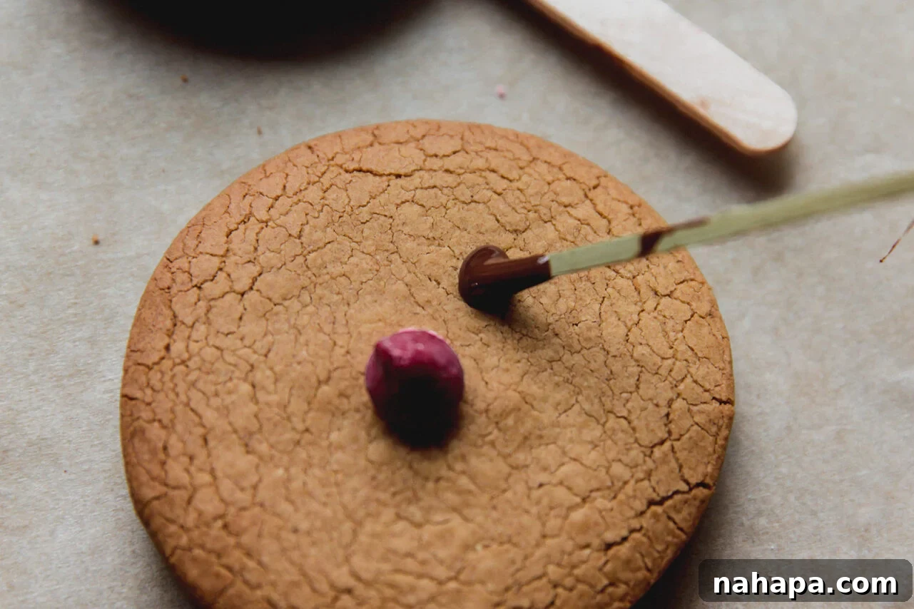 A gingerbread cookie being decorated with a red nose and antlers using melted chocolate, bringing Rudolph to life.